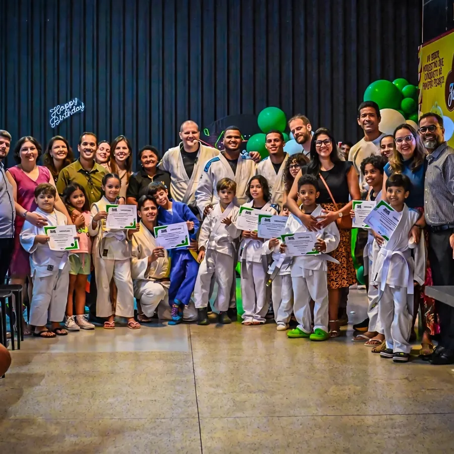 Crianças de kimono com certificados nas mãos, com os pais e a equipe atrás, em cerimônia de graduação