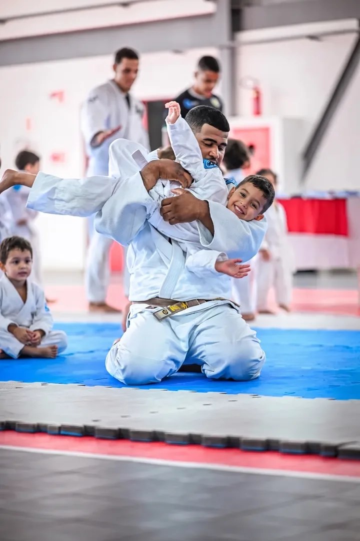 Professor de kimono segurando um aluno sorridente no colo durante o treino
