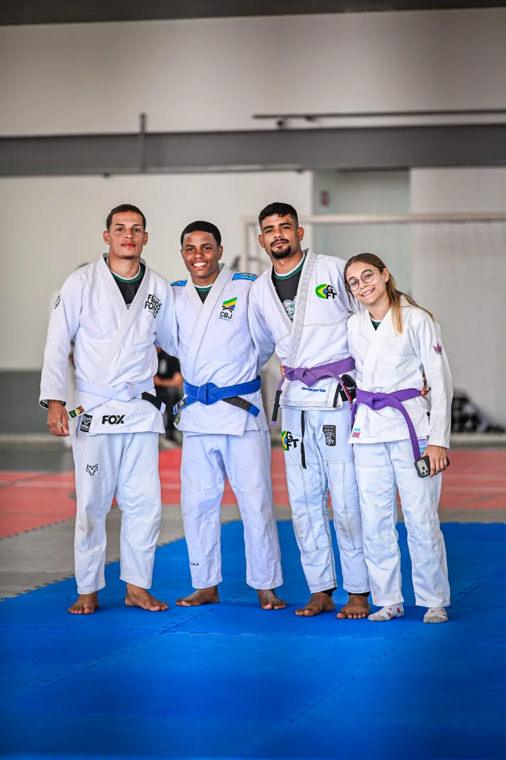 Quatro jovens da equipe, de kimono, lado a lado no tatame