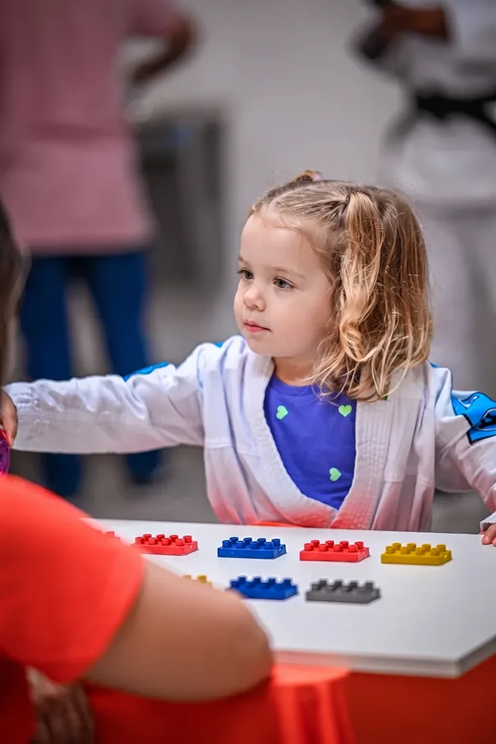 Criança de kimono montando peças coloridas numa mesa de atividades