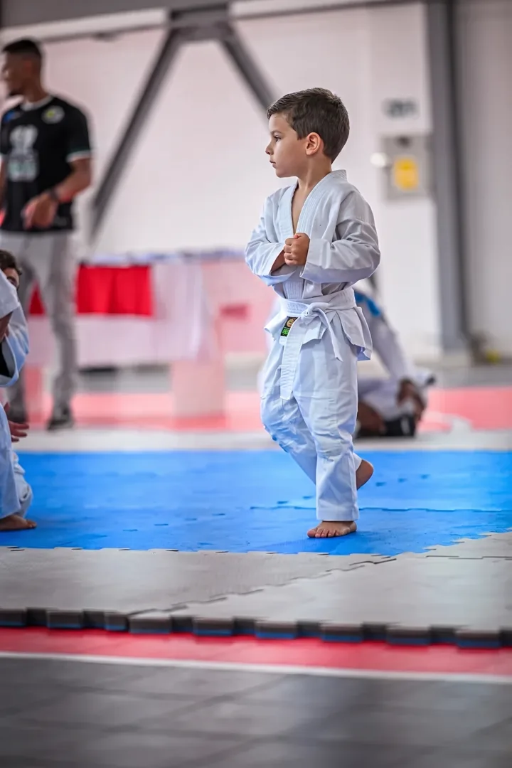 Criança de kimono atravessando o tatame, com professores ao fundo