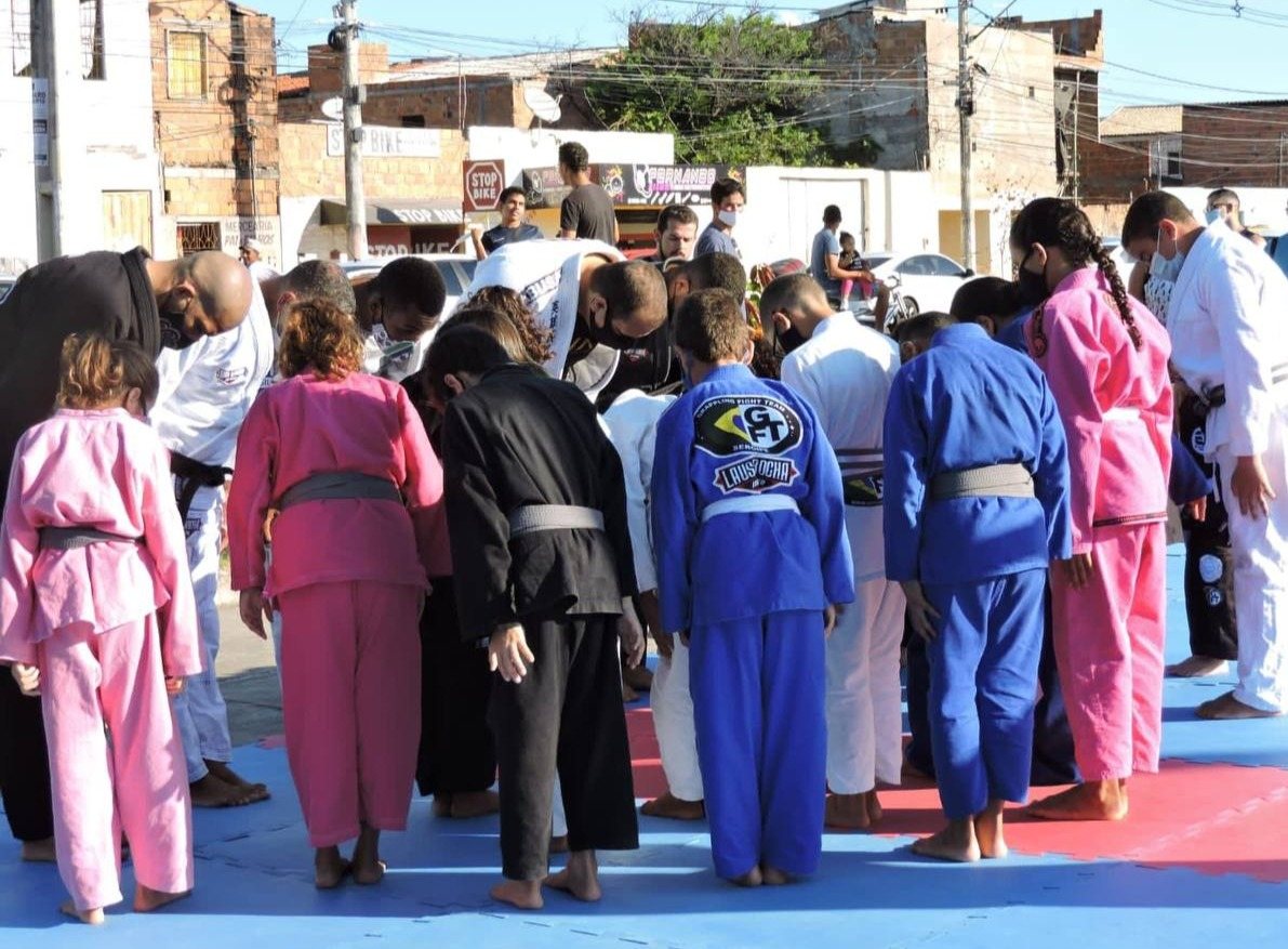 Turma de crianças de kimono em roda no tatame, com os professores